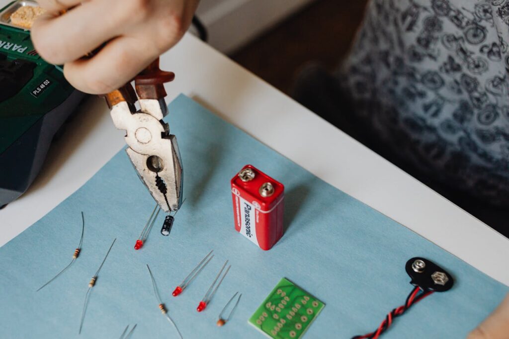 Close-up of electronics repair using pliers with resistors and battery.