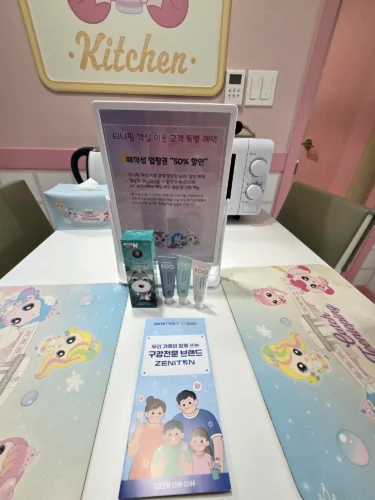 한화리조트 용인 티니핑 객실의 식탁과 전자레인지, 째깍섬 할인 안내판 및 어린이 치약 샘플
